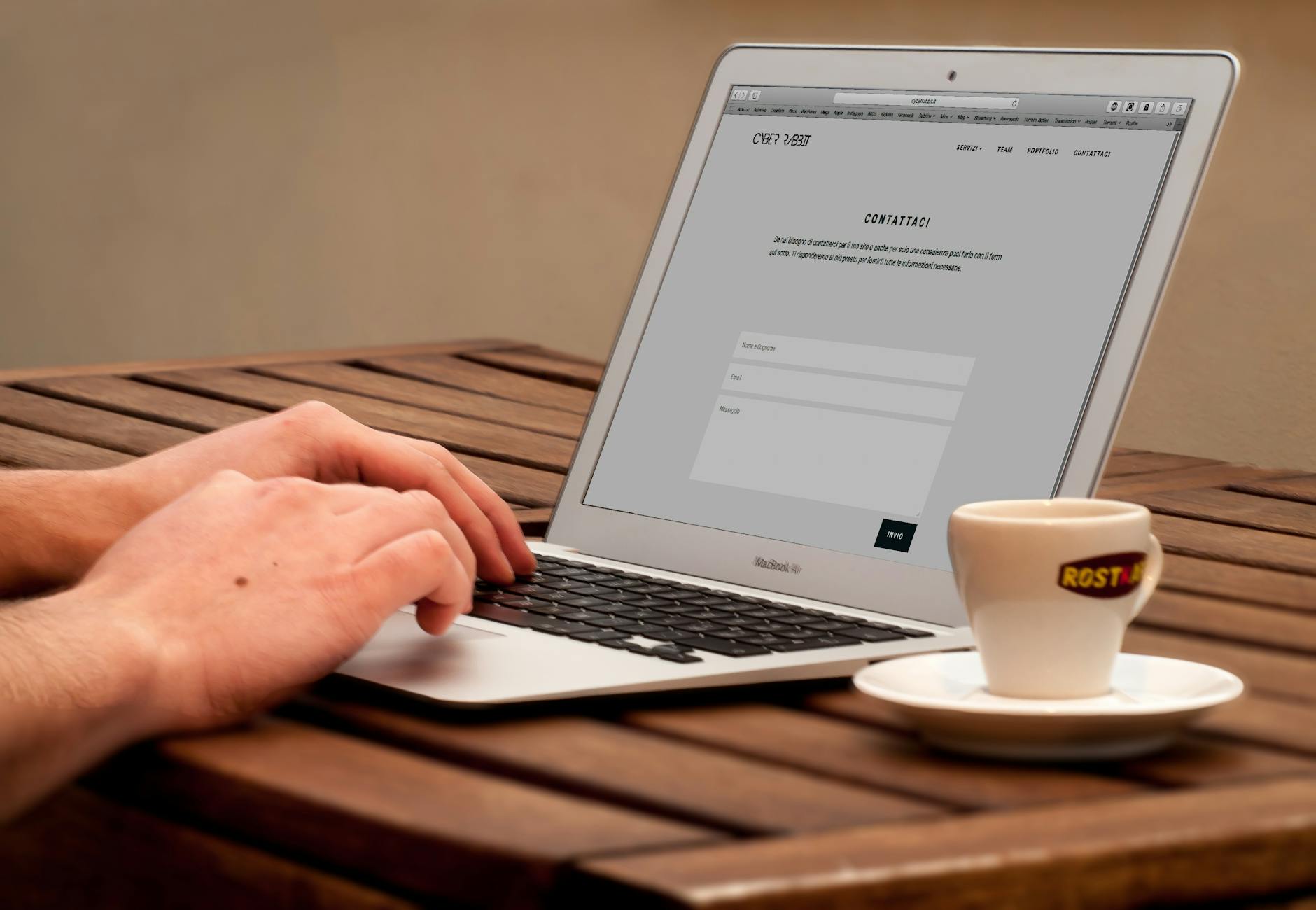human using laptop beside teacup on the wooden table